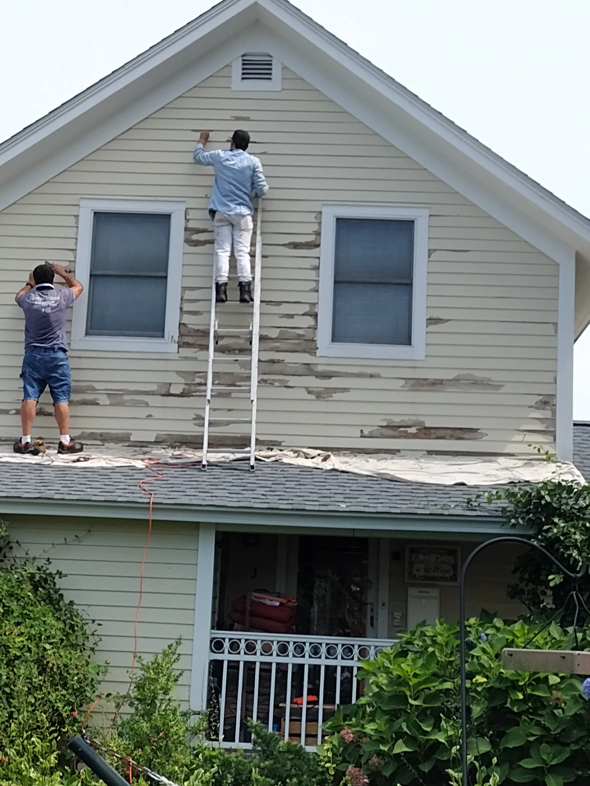 Crew scraping old paint from the gable of a house